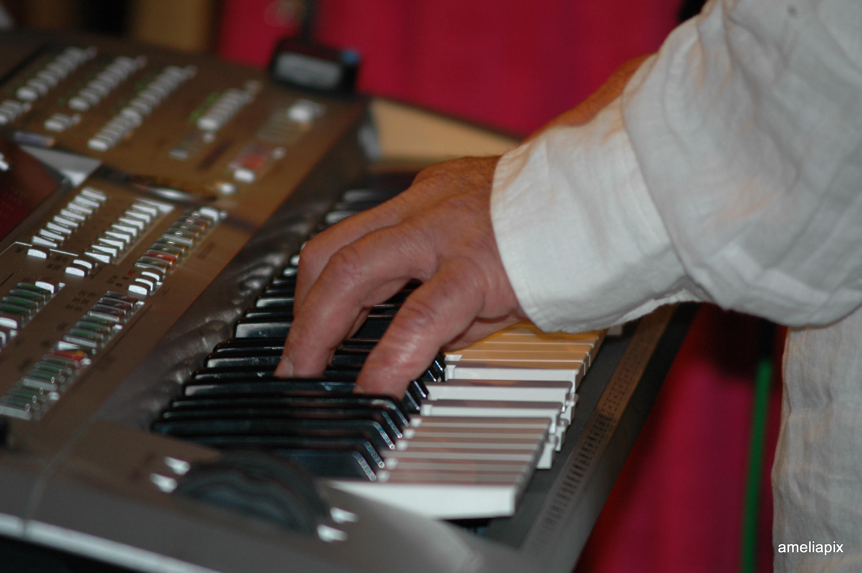 Tony Sheppard's hands on a silver synthesizer keyboard viewed in profile.