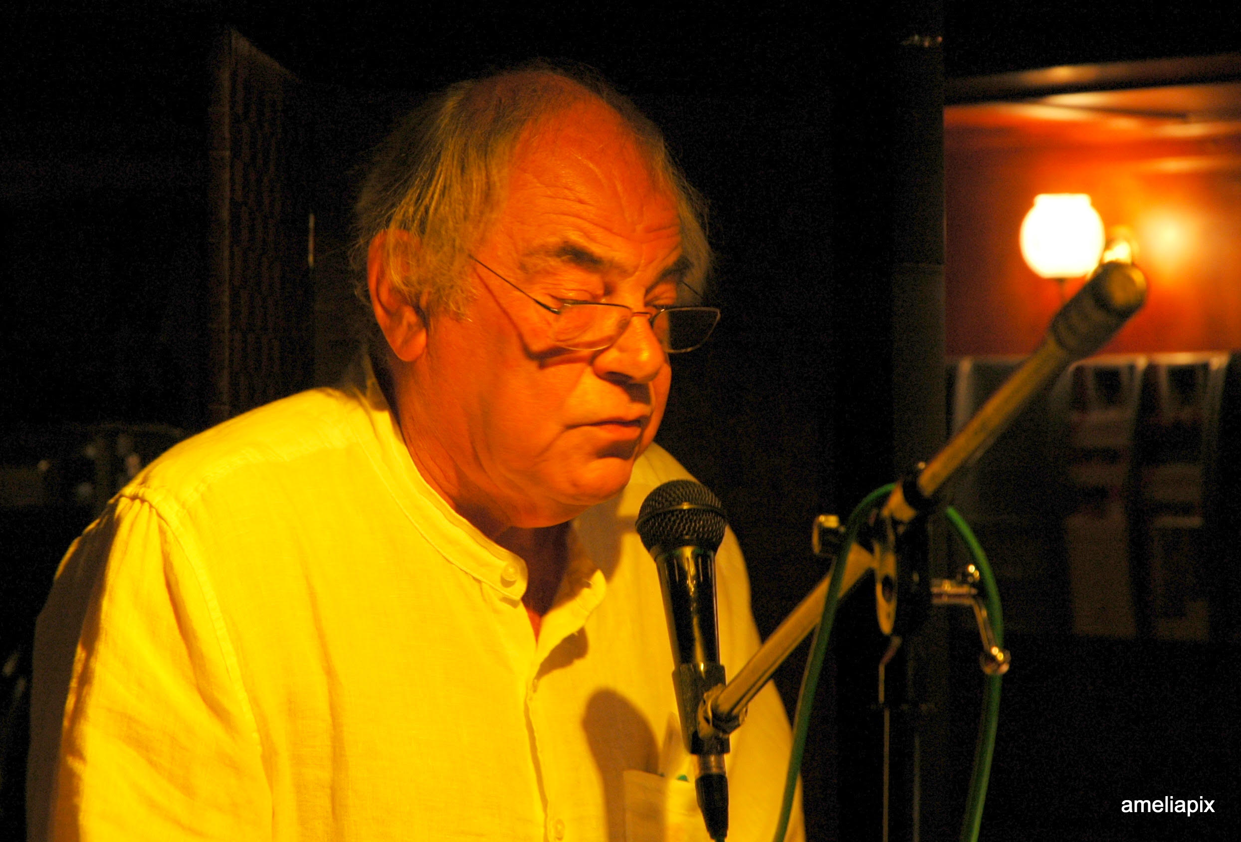 Tony Sheppard sitting at a microphone in a dimly lit nautical space.